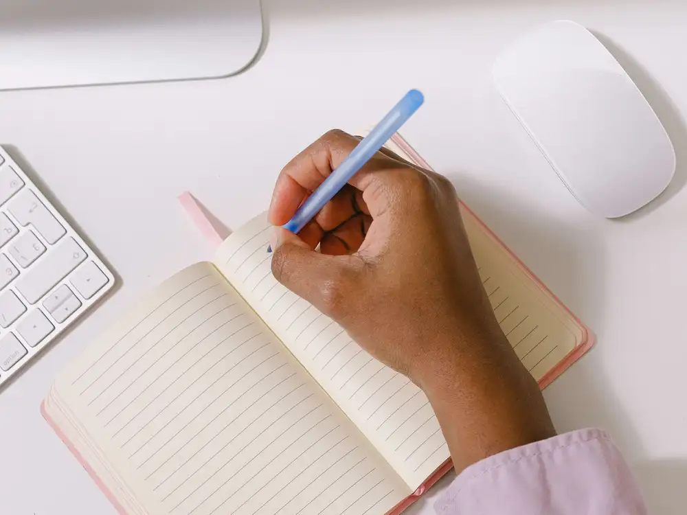 A man writing in a journal on a desk with a computer keyboard and mouse either side